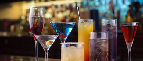 Un bar con varios vasos de bebidas, incluyendo cócteles y una opción sin alcohol, sobre un fondo desenfocado de estanterías.