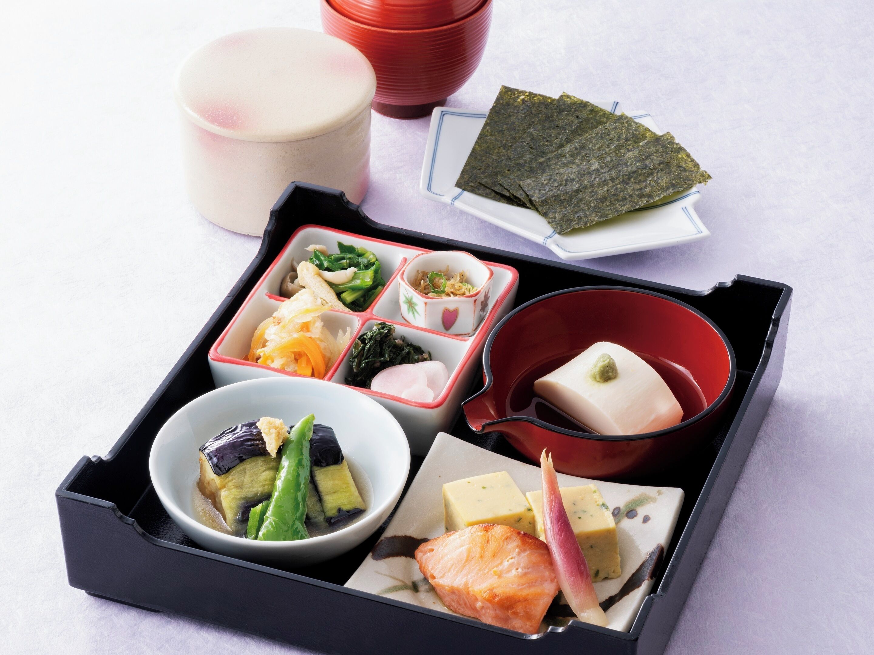 Una caixa de bento amb diversos aliments, com ara peix, verdures i tofu.