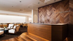 Un área de recepción con mostrador de madera, pared con patrón de espiga y zona de estar con sillas y una mesa.