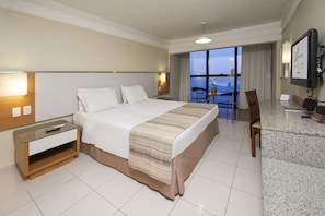 Quarto de hotel com uma cama grande, uma escrivaninha com um computador, uma cadeira e vista para o exterior.