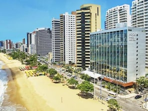 Um hotel na praia com vários edifícios altos, uma praia de areia e um céu azul límpido.