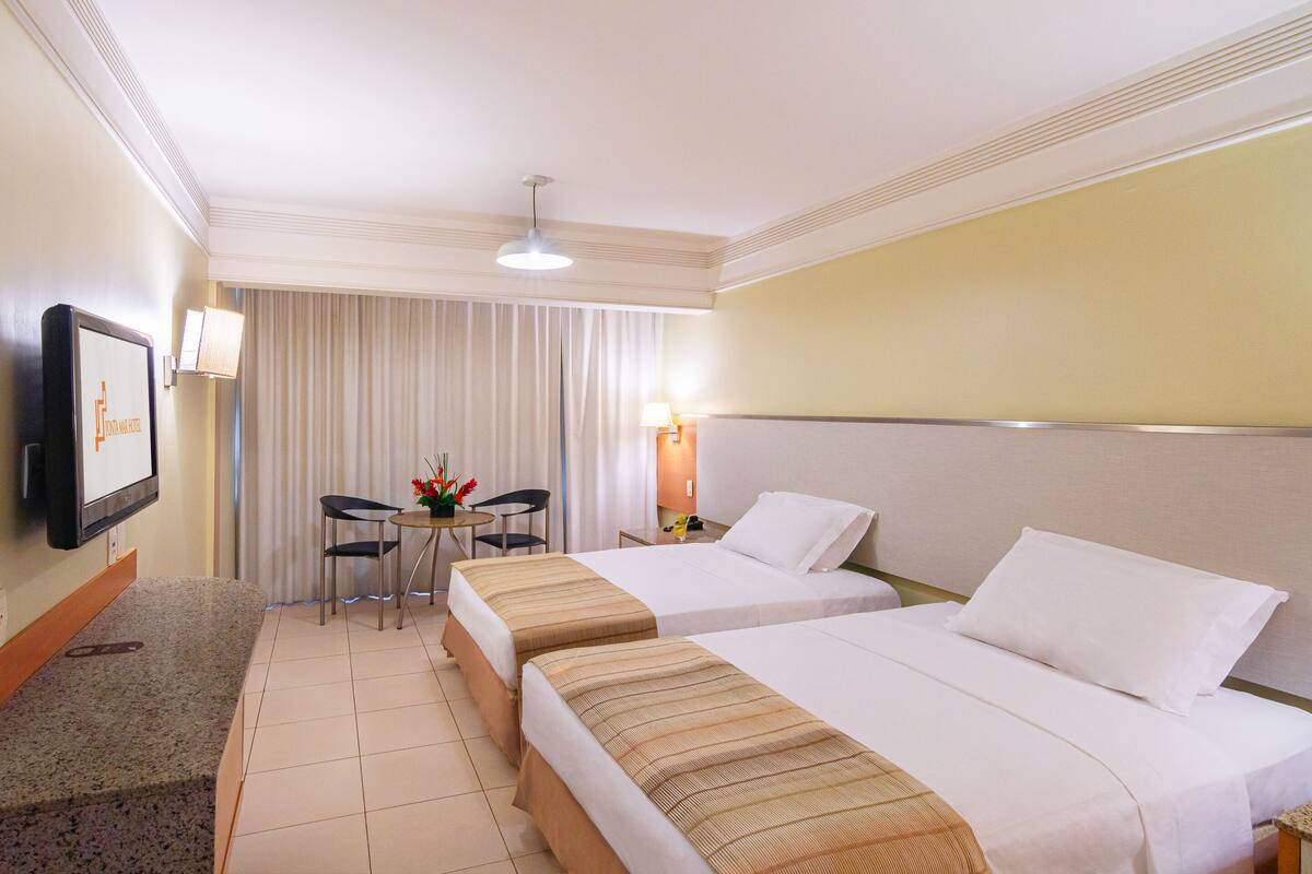 A hotel room with two beds, a desk with a chair, a TV, and a window with curtains.