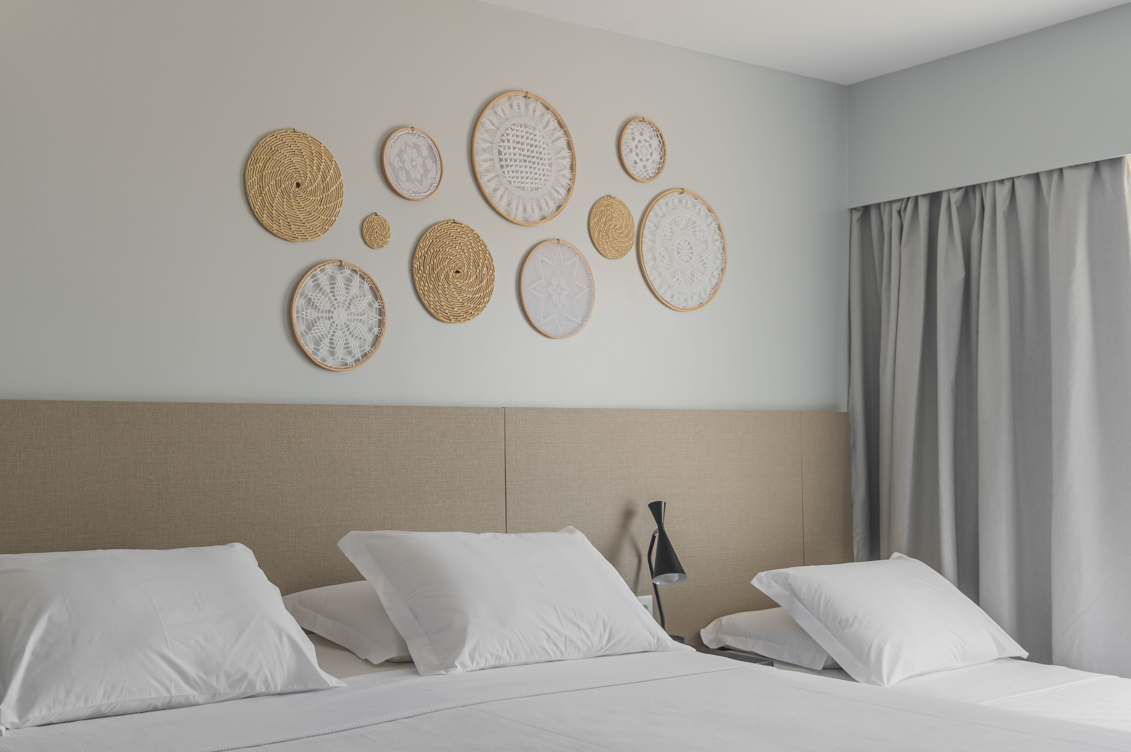 Una habitación de hotel con cama, almohadas, cabecero y un muro con piezas de arte tejidas circulares.