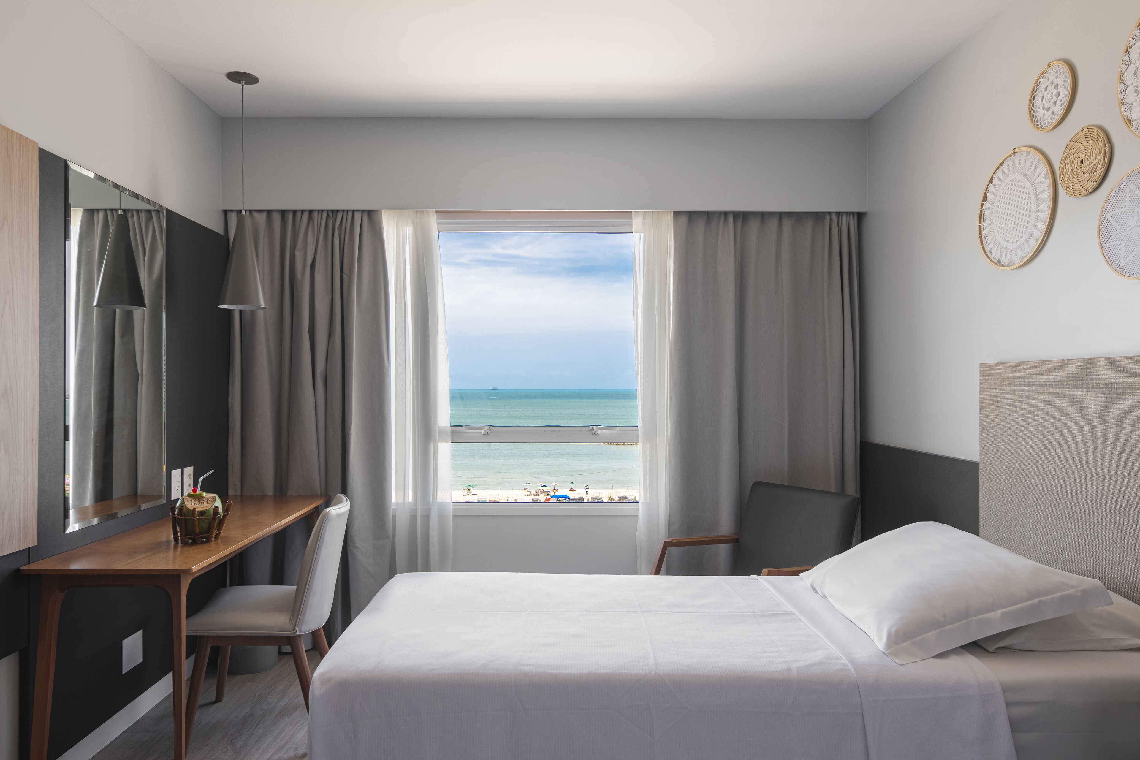A hotel room with a bed, a desk, and a view of the beach.