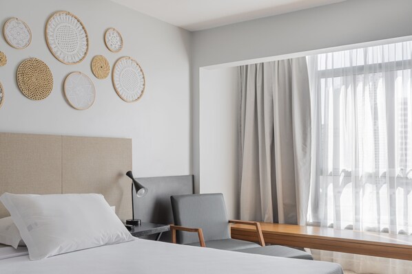 A modern hotel room with a bed, a desk, a chair, and a large window with curtains.