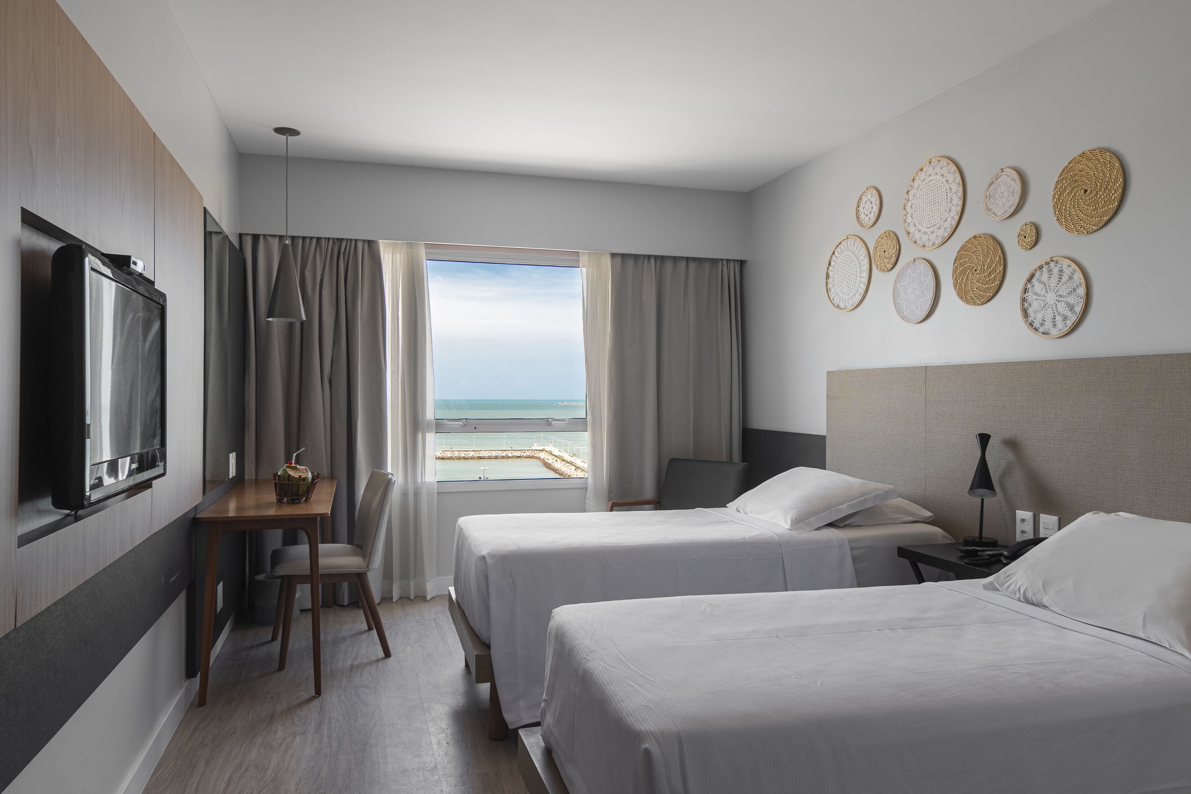 Habitación de hotel con dos camas, televisión, escritorio y silla, y vista al mar.