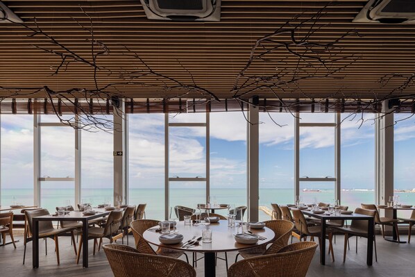 A restaurant with large windows offering a view of the sea. Tables are set with plates, glasses, and cutlery. - Praiano Hotel (Fortaleza)