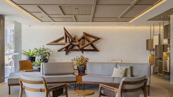 Un hall d’entrée moderne avec un mur en briques blanches, une œuvre d’art géométrique en bois et un espace détente avec des canapés et des fauteuils.