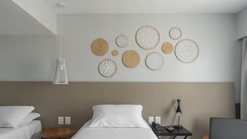 Quarto de hotel com cama, mesas de cabeceira, luminária e arte decorativa na parede.