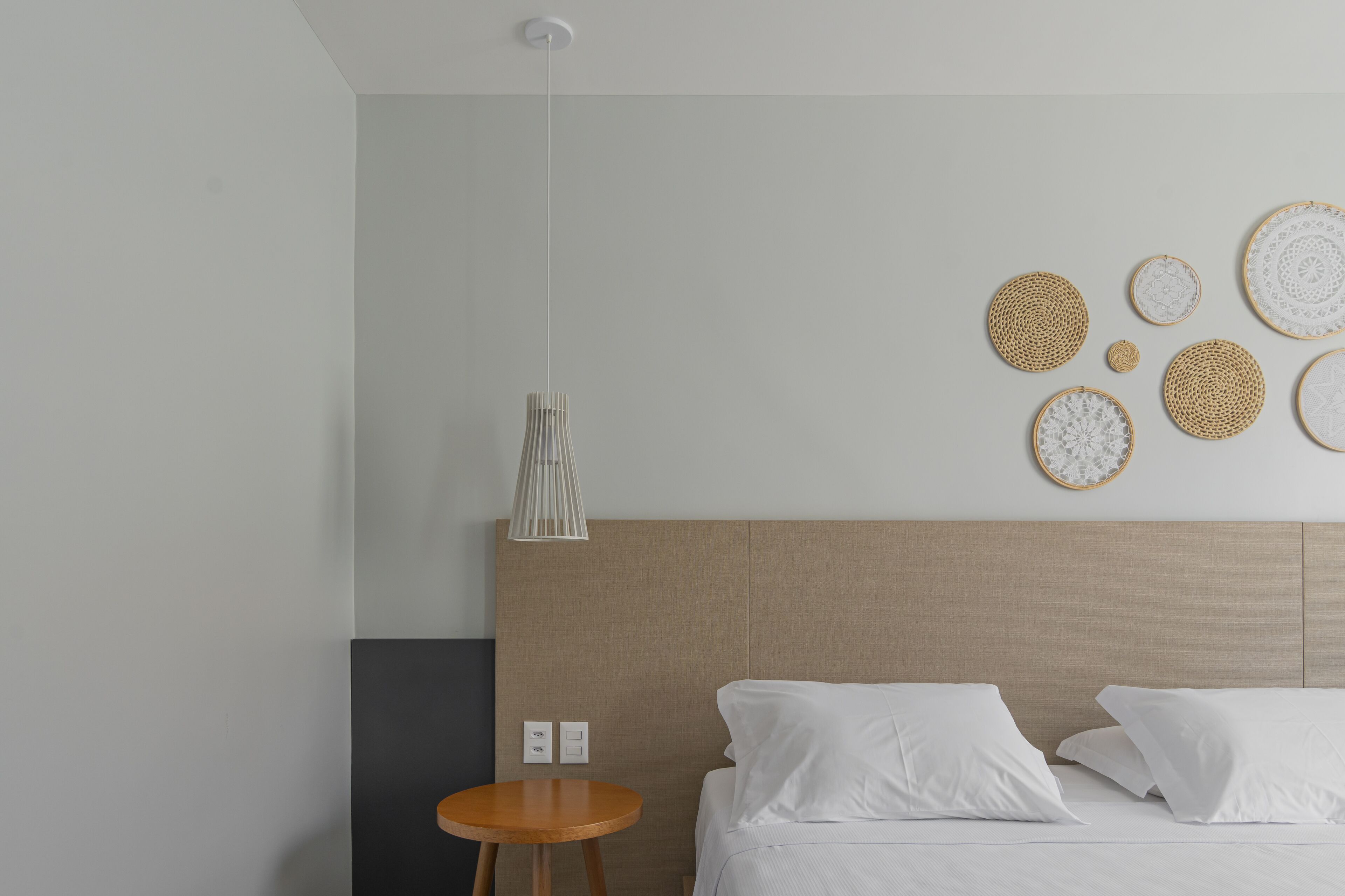 A modern hotel room with a bed, a round wooden side table, and wall-mounted decorative items.
