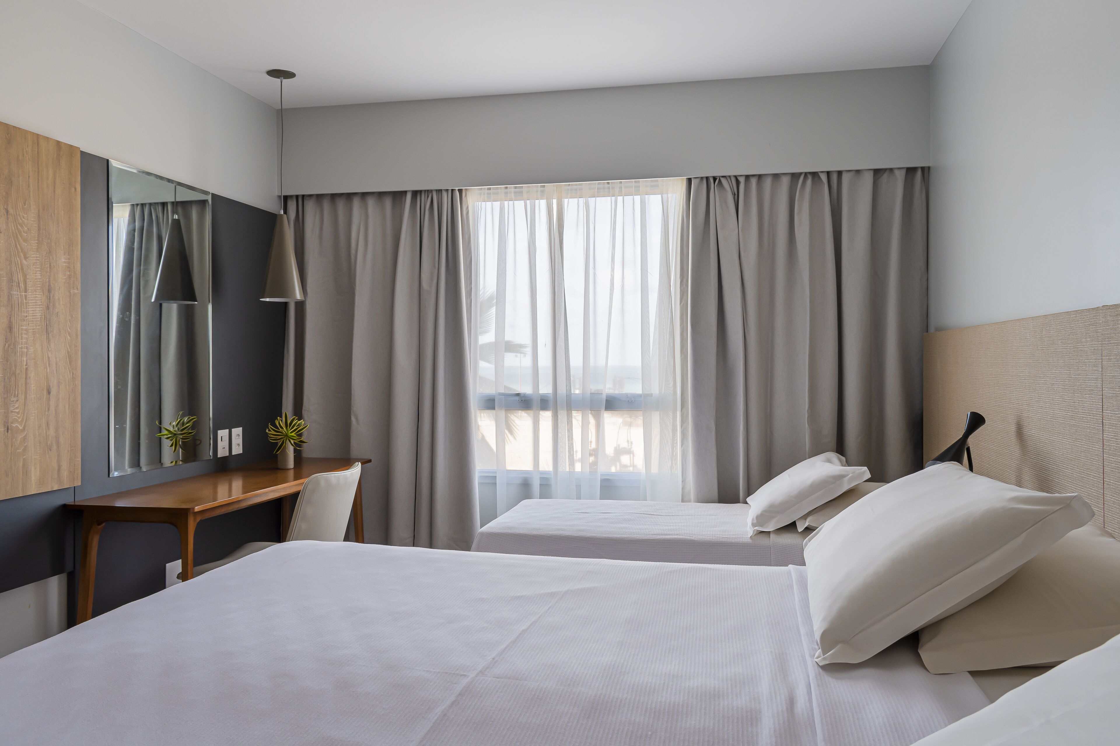 A hotel room with two beds, a desk, and a large window with curtains.