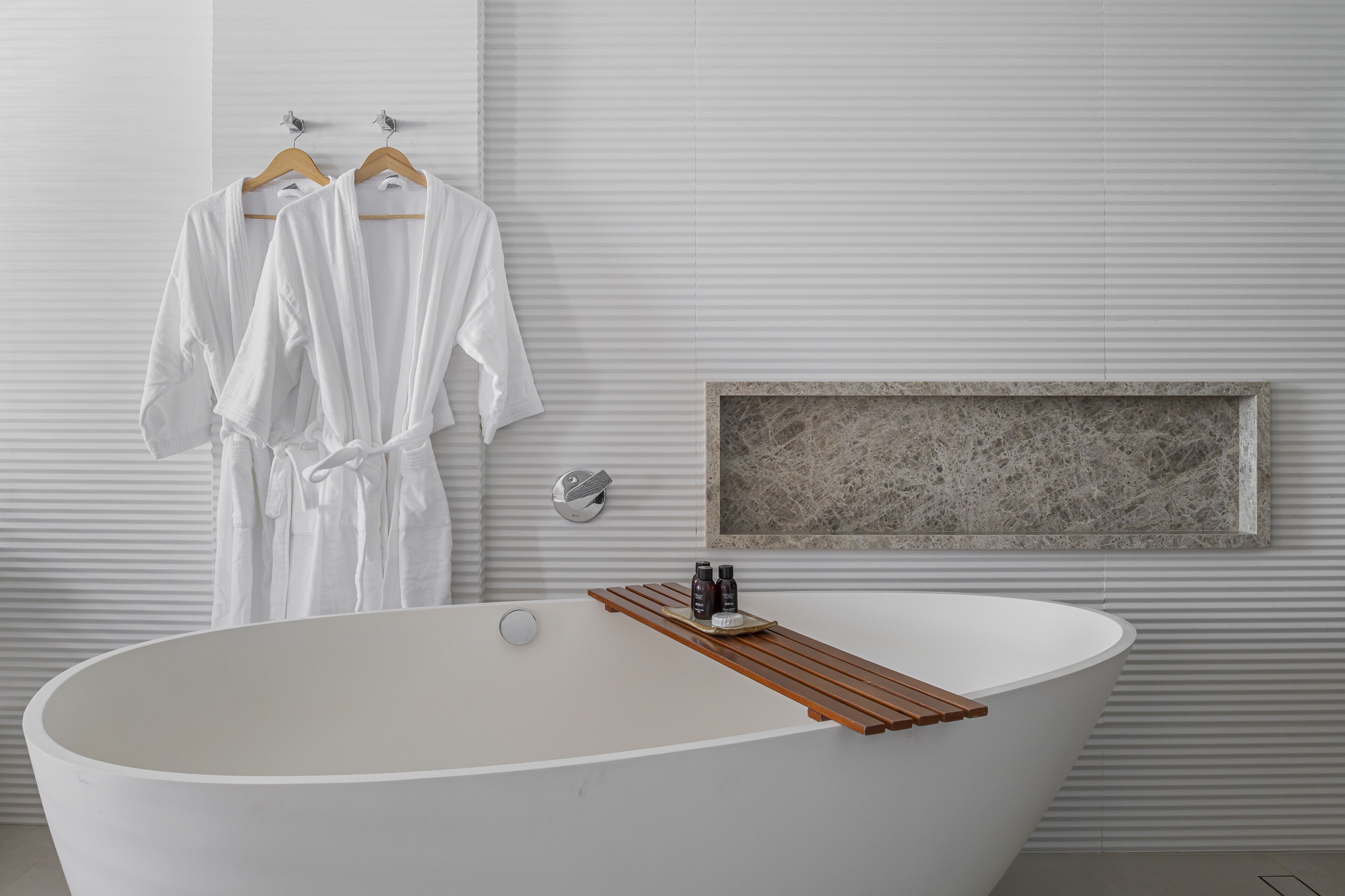A modern bathroom with a freestanding bathtub, wooden bath mat, and a marble-framed mirror.
