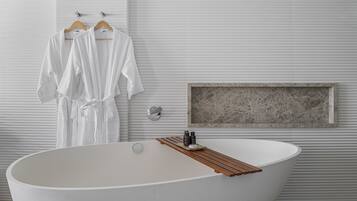A modern bathroom with a freestanding bathtub, wooden bath mat, and a marble-framed mirror.