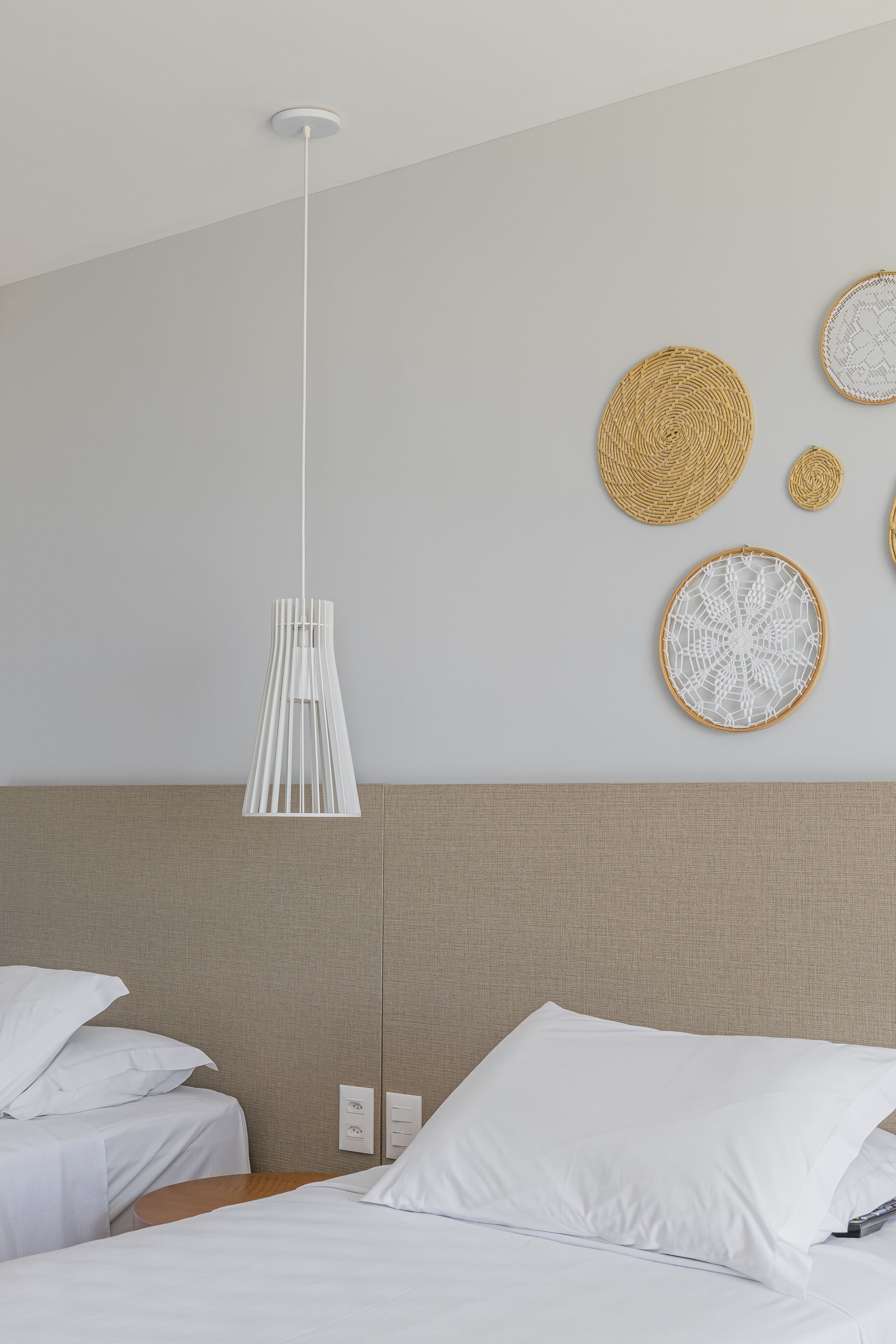 Une chambre d’hôtel moderne, équipée d’un lit, de deux tables de chevet, d’un luminaire fixé au mur et d’une décoration murale tissée.