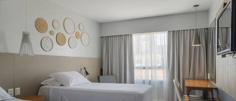 Una habitación de hotel con dos camas, un escritorio y un ventanal con cortinas.