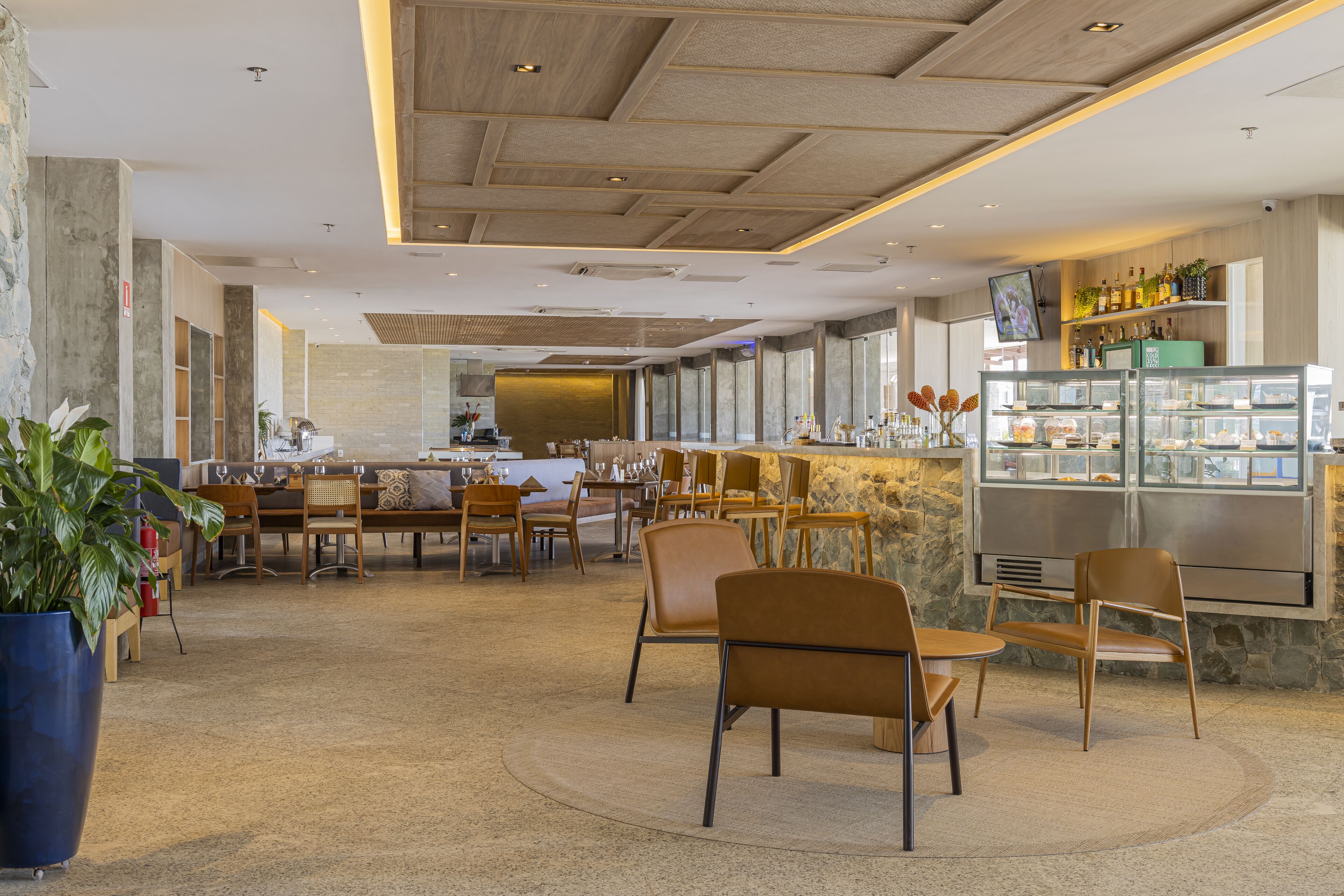 A modern restaurant interior with a central bar area, seating arrangements, and a display case with food items.