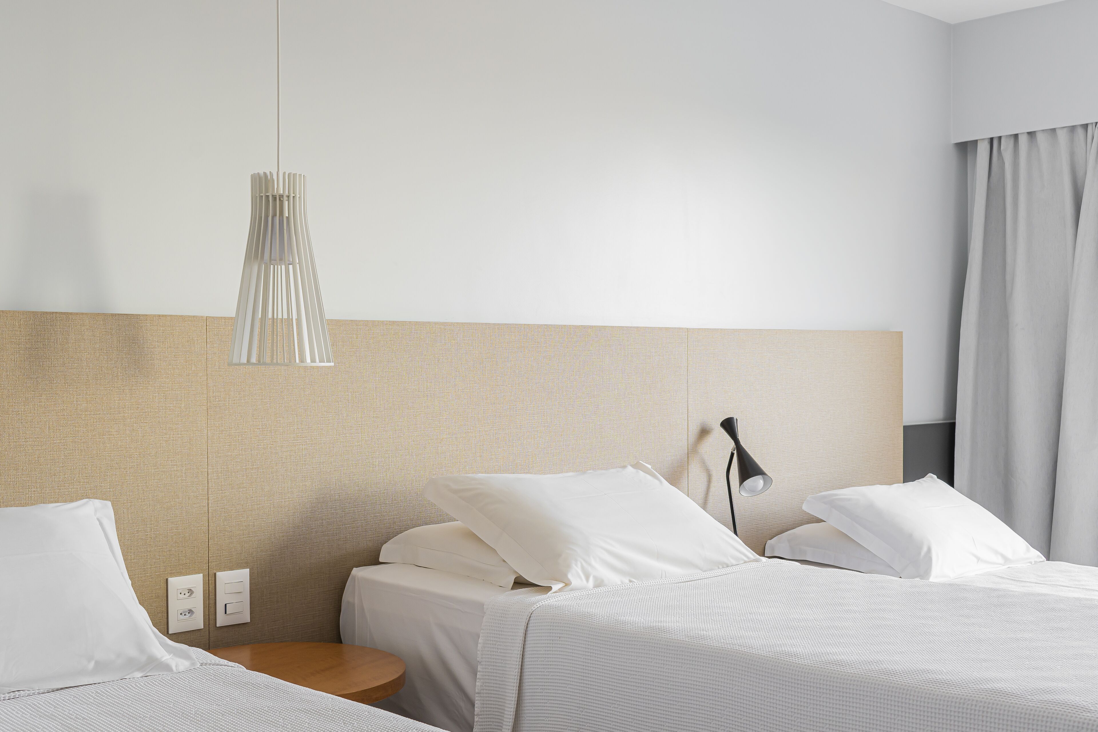 A hotel room with two beds, a bedside table, a lamp, and a hanging light fixture.