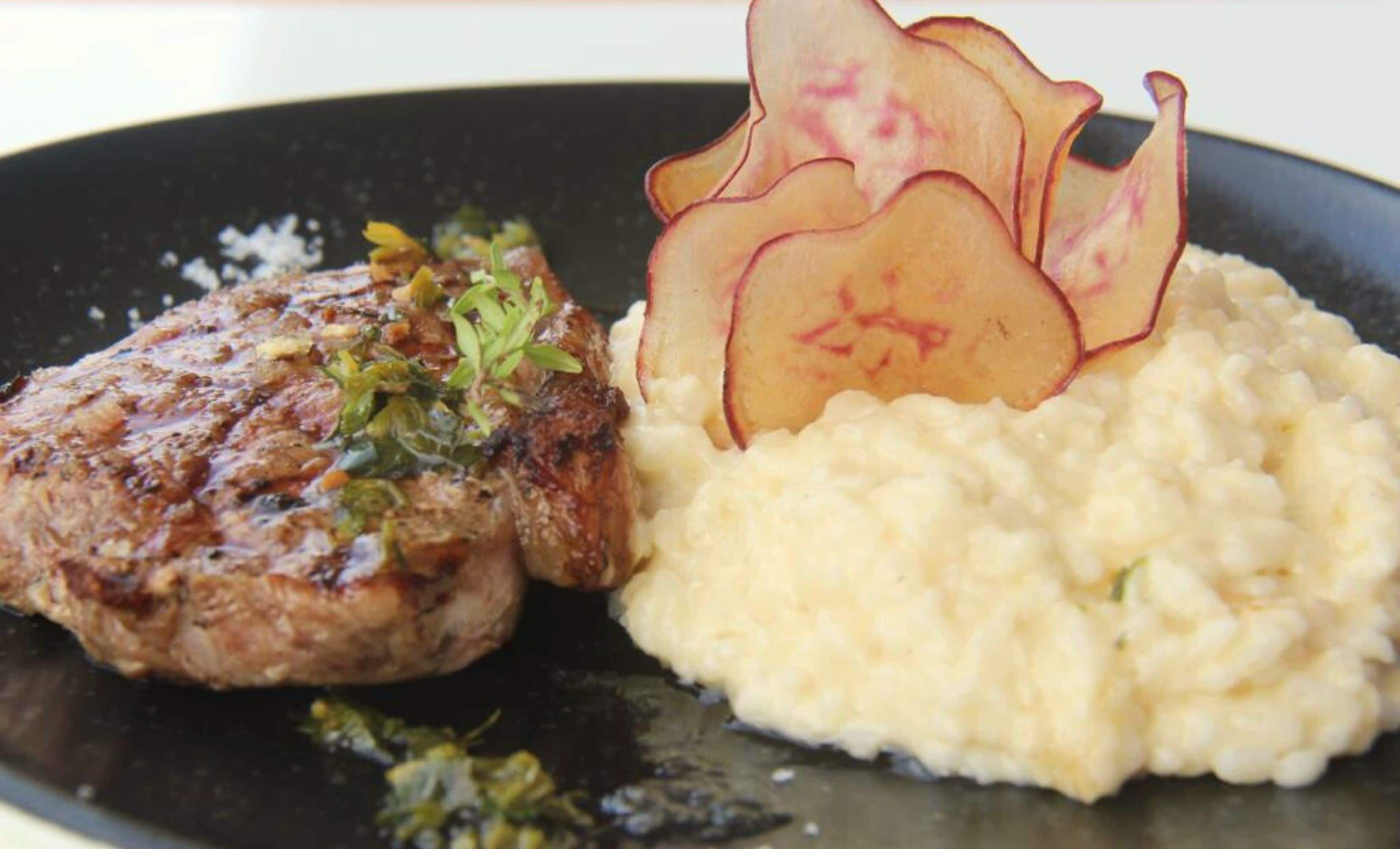 Un plato con un bistec a la parrilla, puré de papas y una rodaja de manzana decorativa.