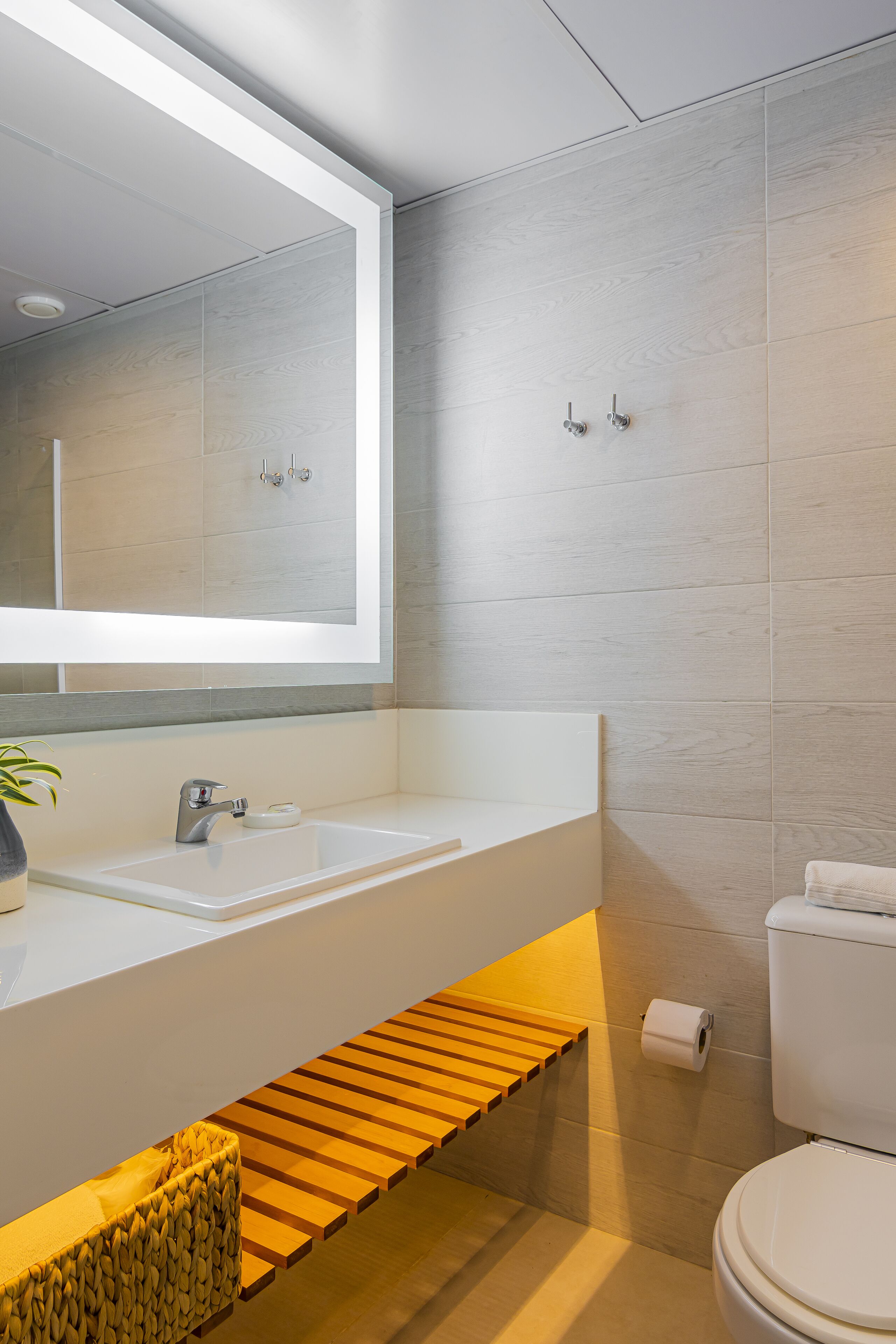 Une salle de bain moderne avec un lavabo blanc, un grand miroir et une étagère en bois.