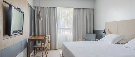 Habitación de hotel con cama, escritorio, silla, televisor y ventana con cortinas.