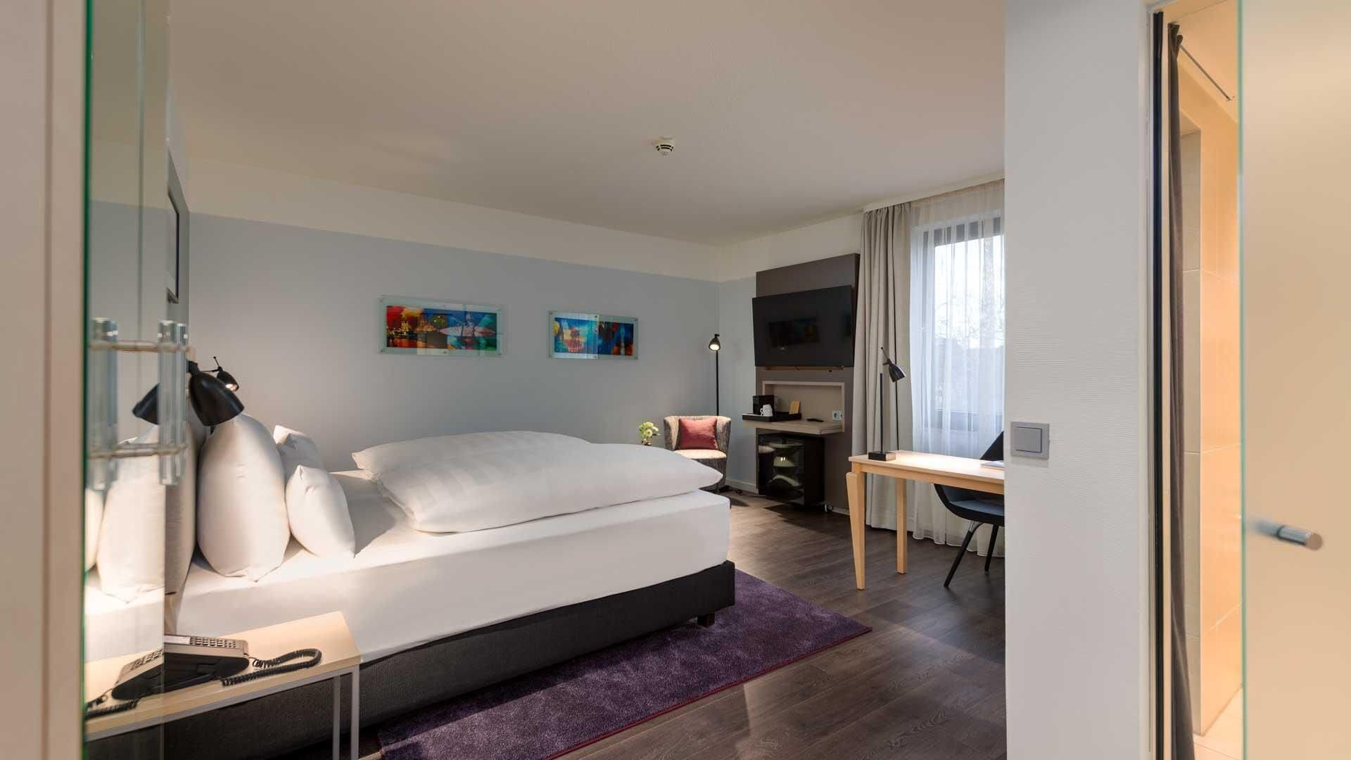 Una habitación de hotel moderna con cama, escritorio y dos cuadros en la pared.
