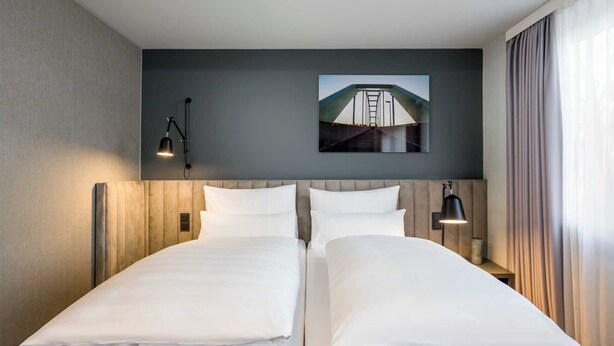 A hotel room with two beds, a dark wall, a framed picture, and a window with curtains.