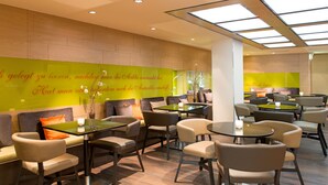 A modern restaurant with a green wall featuring text, multiple seating areas with tables and chairs, and a high ceiling with skylights.