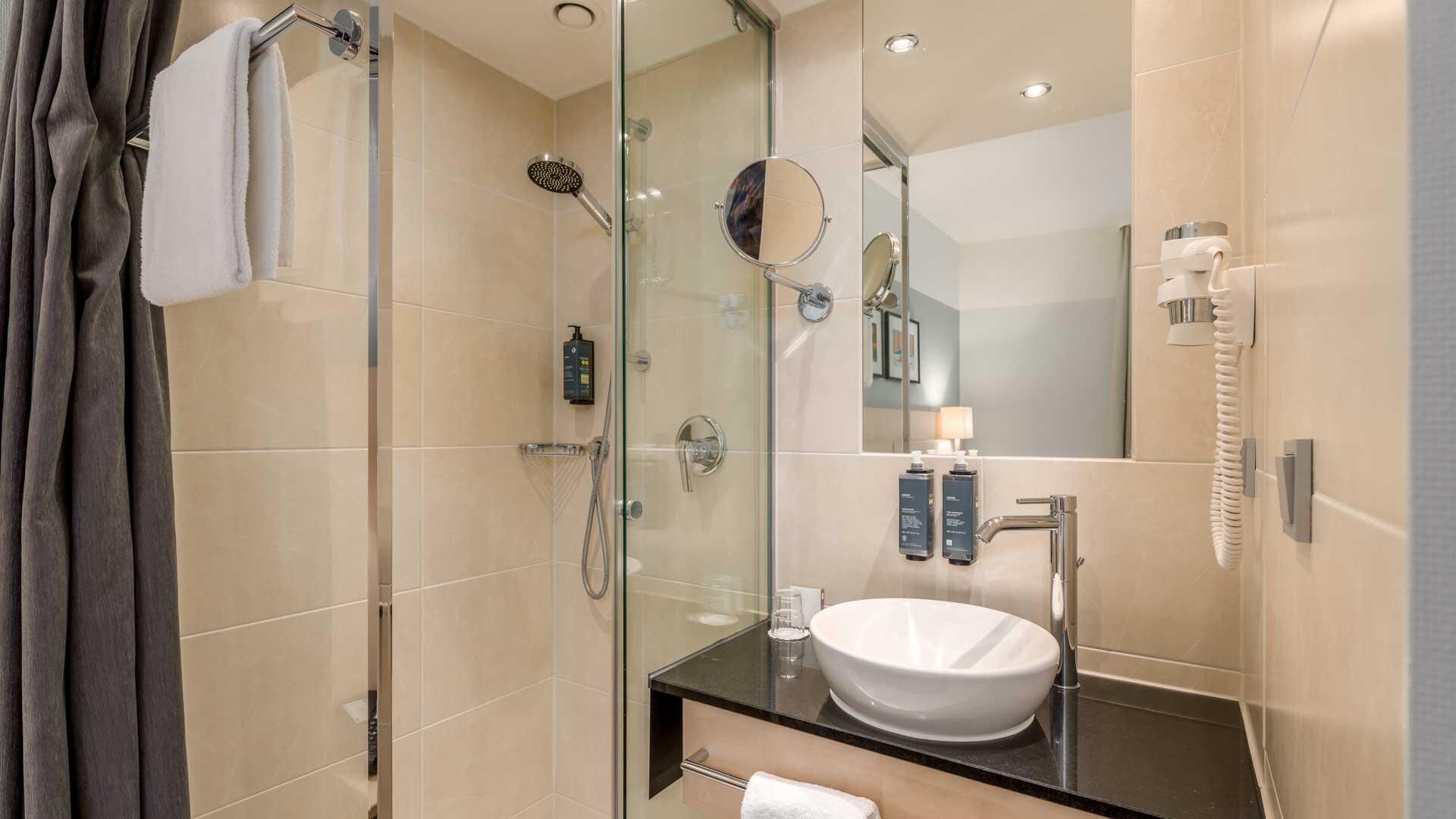 Een moderne badkamer met een douche met glazen wand, een wastafel met een witte wasbak en een spiegel.