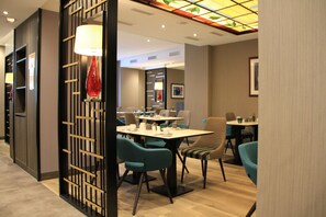 Un comedor moderno con sillas color turquesa, una mesa central y un jarrón decorativo rojo.