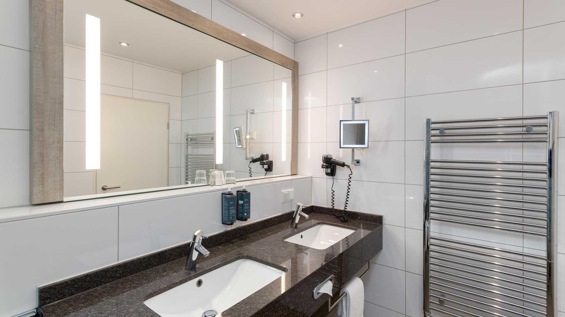 A modern bathroom with two sinks, a large mirror, and a towel rack.