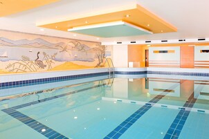 Ein moderner Innenpool mit klaren blauen Fliesen, einer Wandmalerei mit Vögeln und Bergen sowie einem Empfangsbereich mit einer Holzvertäfelung.