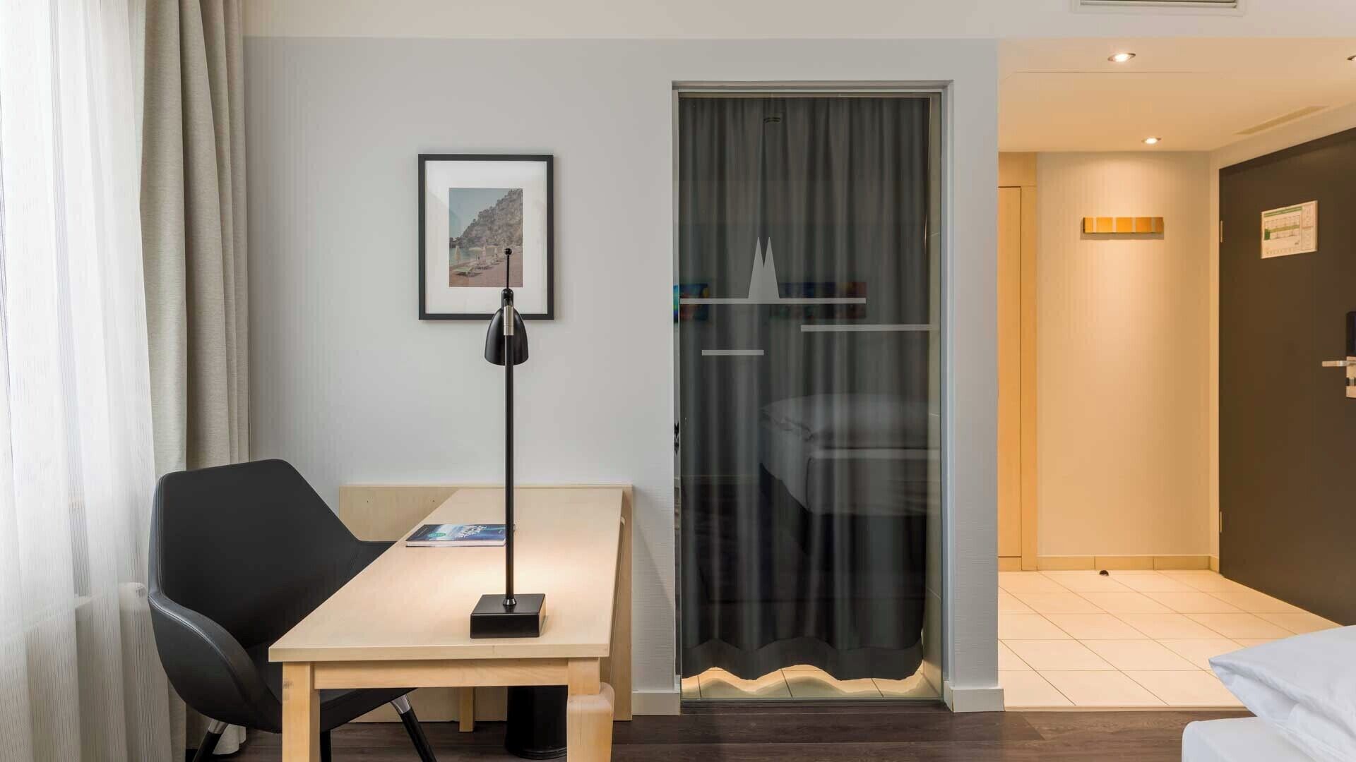 A hotel room with a desk, chair, and a large window with curtains.