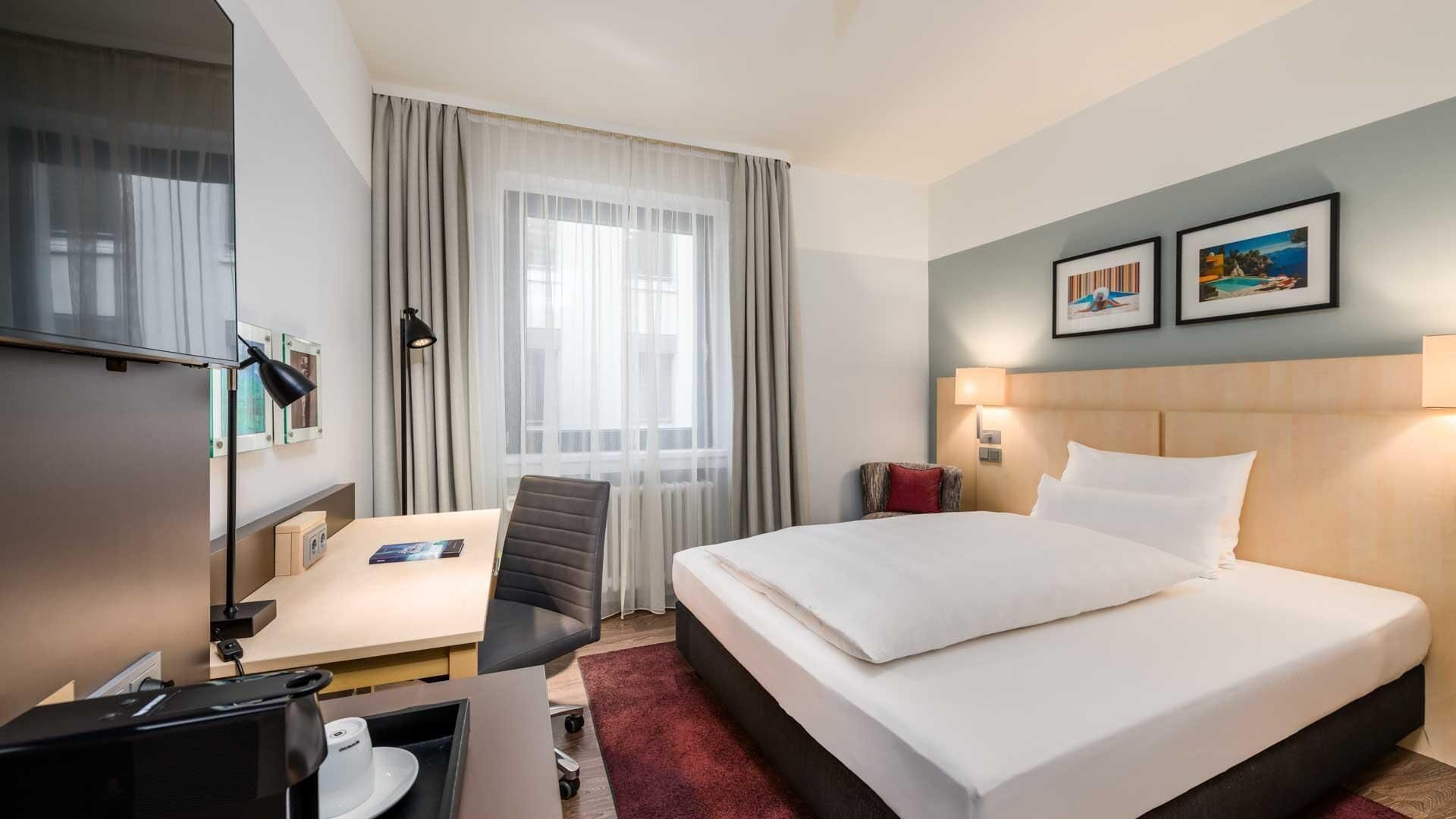 Ein Hotelzimmer mit Bett, Schreibtisch, Stuhl und einem Fenster mit Vorhängen.