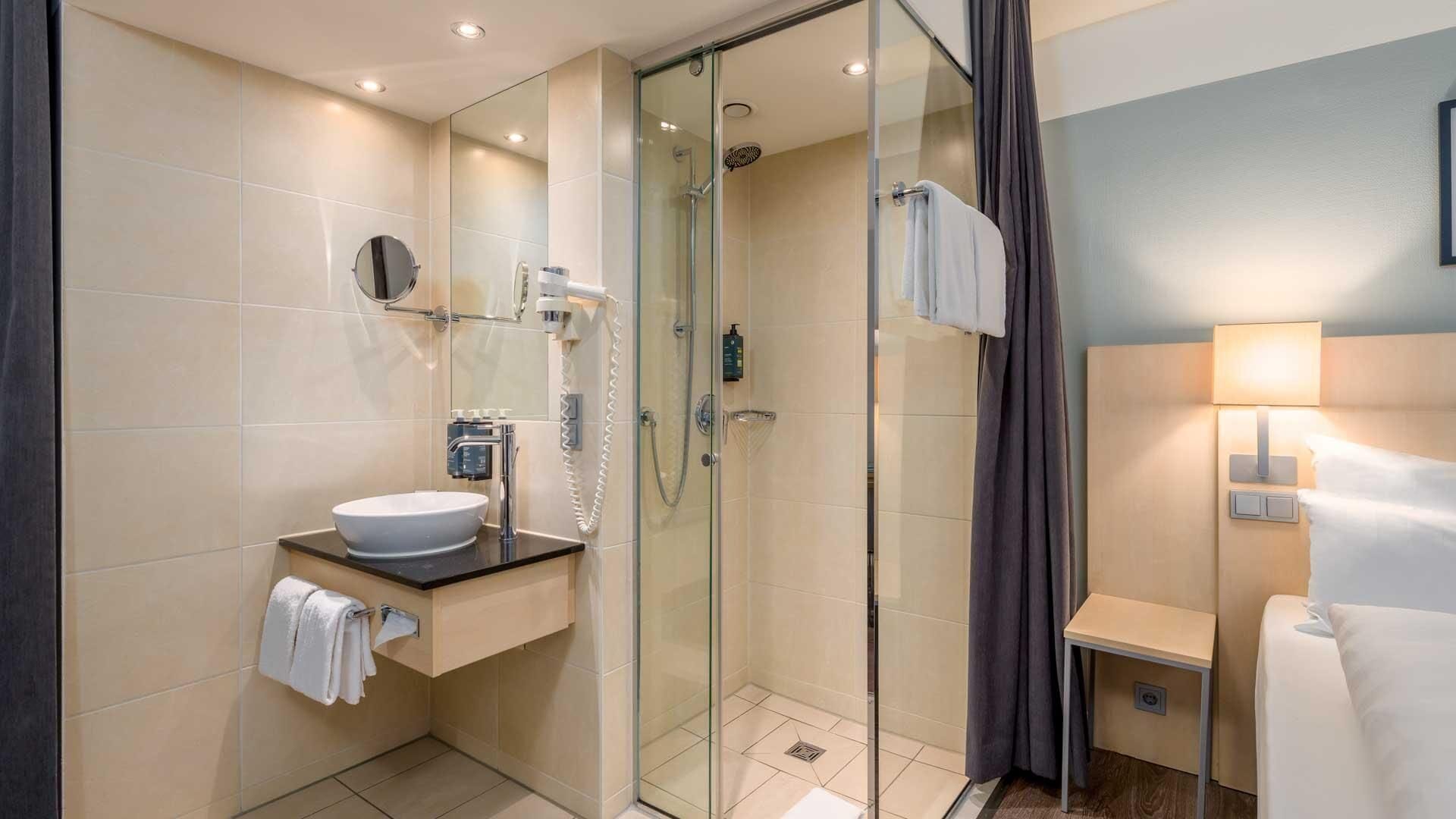 Een moderne badkamer met een douchecabine van glas, een witte wastafel en een handdoekrek.