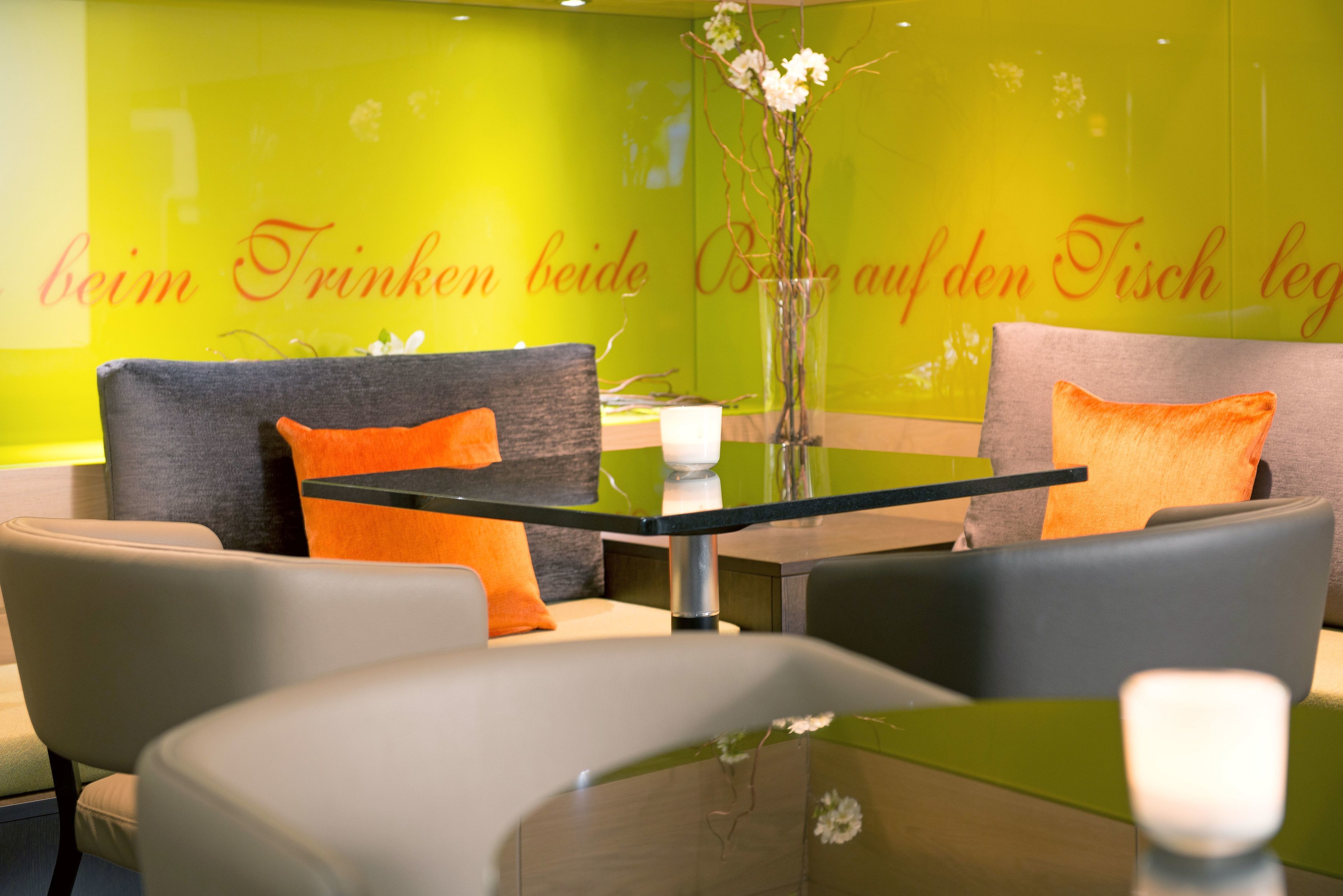 A modern hotel lobby with a green wall, a glass table, and comfortable seating.