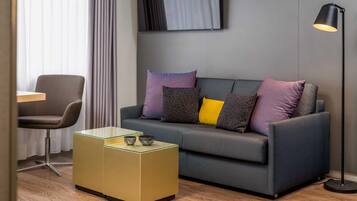 A modern living room with a grey sofa, a glass coffee table, a black floor lamp, and a grey armchair.