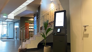 A modern lobby with a staircase, a digital kiosk, and a potted plant.