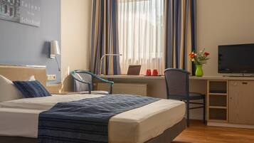 Habitación de hotel con cama, escritorio, silla, televisor y ventana con cortinas.