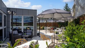 Un patio al aire libre con mesas, sillas, sombrillas y plantas en macetas.