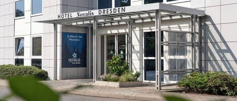 A modern hotel entrance with a glass door and a covered waiting area.