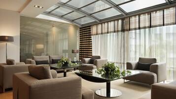 A modern living room with a glass ceiling, large windows with blinds, and a central coffee table with plants.