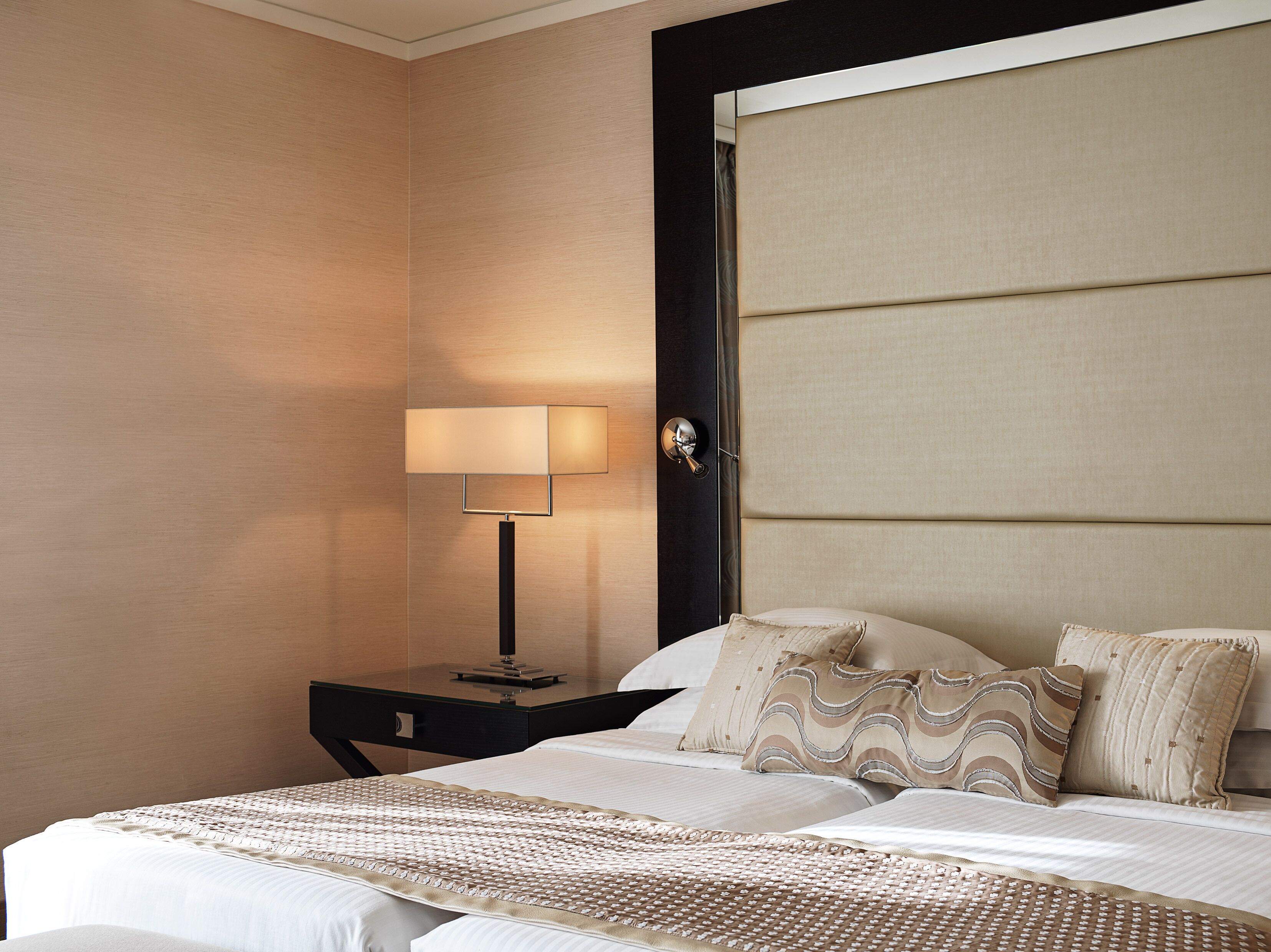 Una habitación de hotel con una cama, una mesita de noche, una lámpara y un cabecero.
