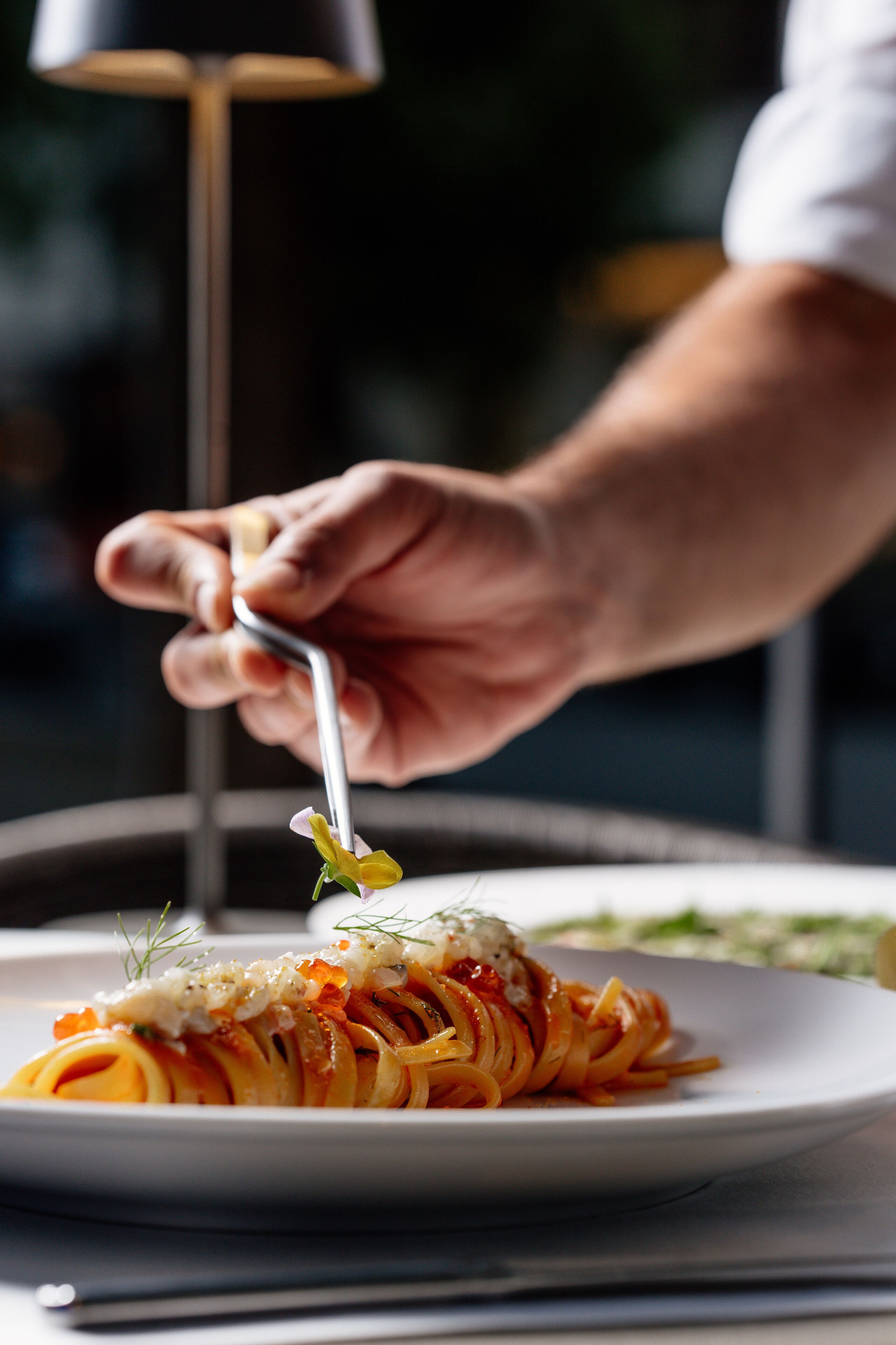 Iemand eet spaghetti met een vork, met garnering op een bord.