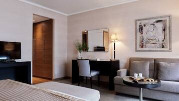 Habitación de hotel con cama, escritorio con silla, sofá, una mesita con bandeja de comida, lámpara y un cuadro en la pared.