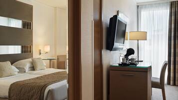 A hotel room with a bed, a desk with a TV, a lamp, and a chair.