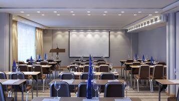 Una sala conferenze con tavoli, sedie e uno schermo per proiezioni.