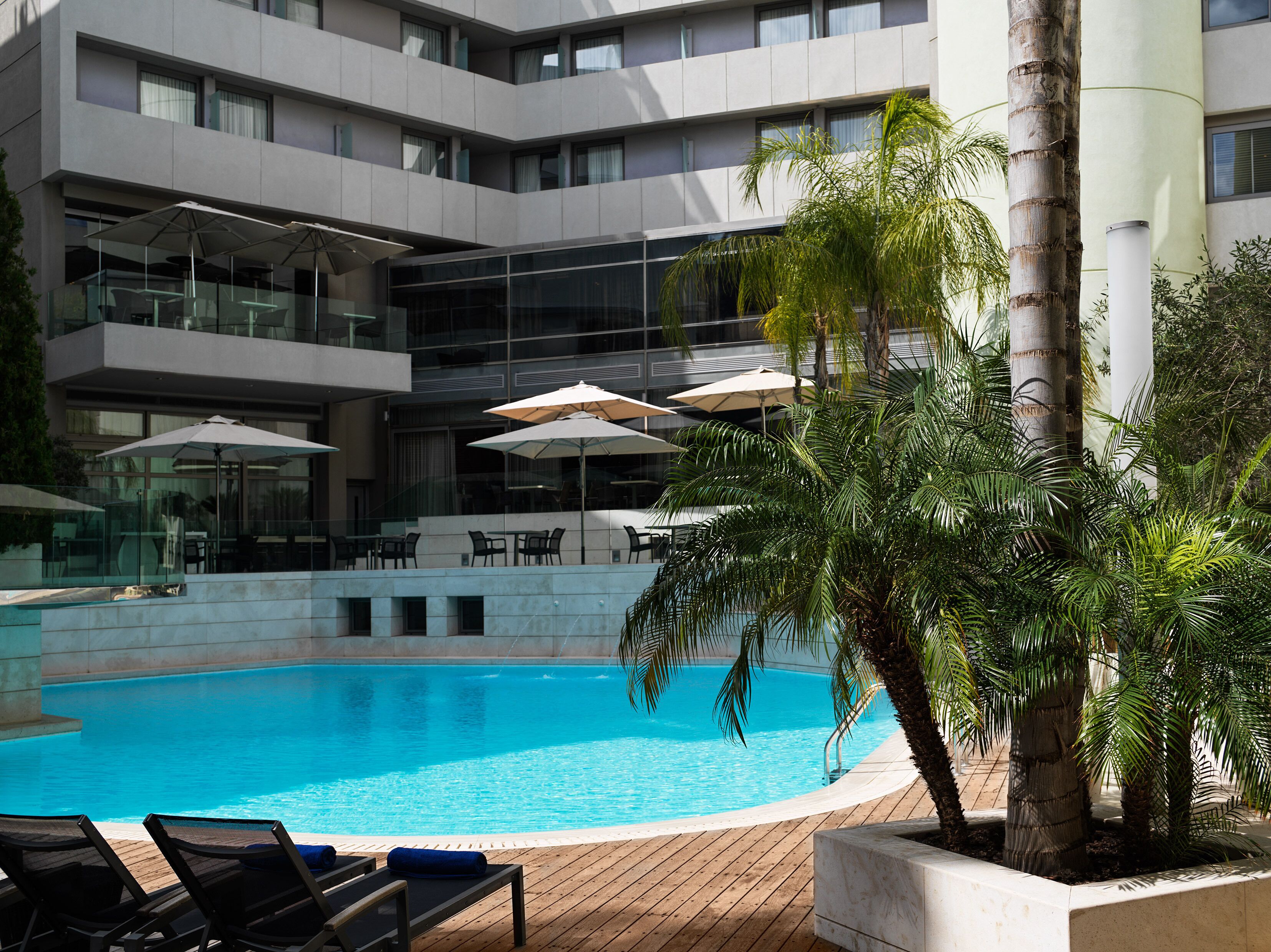 Un hotel moderno con piscina, mesas al aire libre y palmeras.