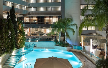 A modern hotel with a central swimming pool, multiple balconies, and outdoor seating areas.