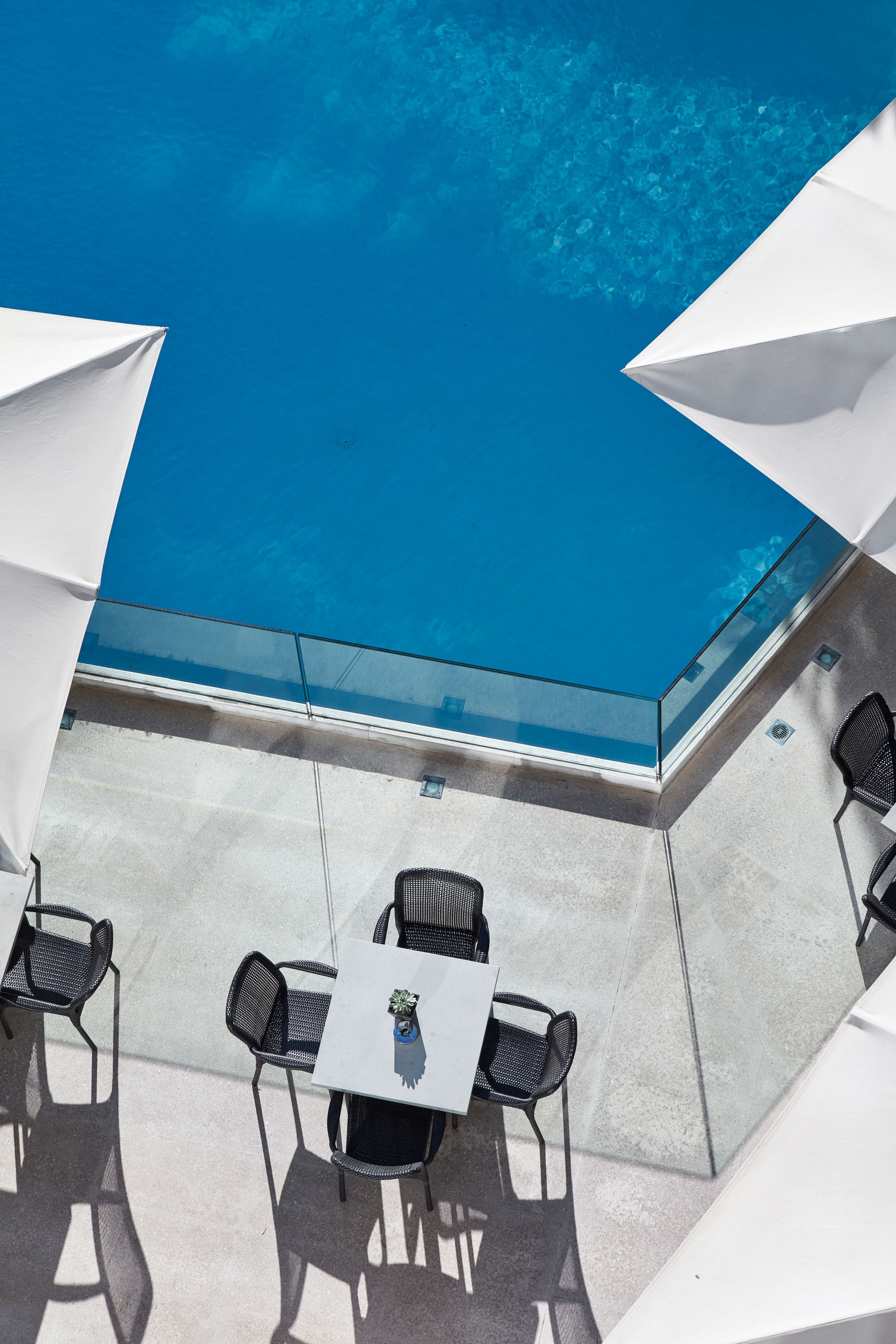 Terraza en la azotea con barandilla de cristal que da a una piscina, amueblada con mesas y sillas.
