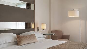 A hotel room with a large bed, a bedside table, a chair, a floor lamp, and a mirror.